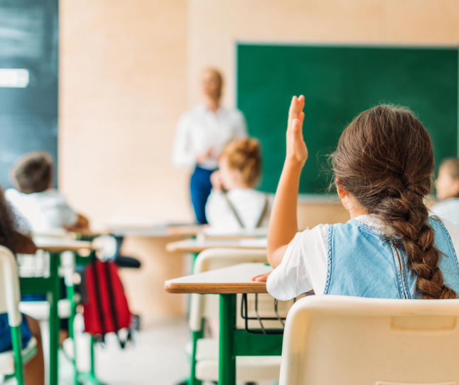 girl raising hand in classroom to answer question